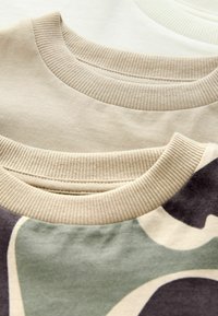 Trois encolures de sweatshirts dans des teintes variées : crème clair, beige-tan et un motif camouflage. Poignets côtelés avec une texture douce, vue en gros plan.