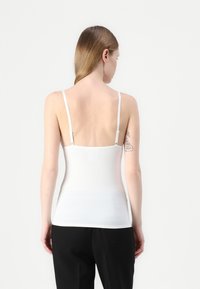 White stretch camisole with thin adjustable straps, seamless design, smooth texture, and a fitted silhouette. No visible logos or patterns.