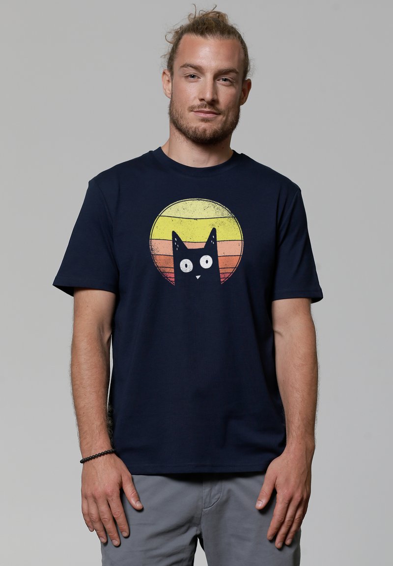 T-shirt en coton bleu marine avec un graphisme d'un chat noir sur un motif de cercles jaunes et orange usés. Manches courtes, col rond.