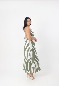Abito maxi con un motivo ondulato verde e bianco, realizzato in tessuto morbido, con un design elegante sulla schiena e spalline sottili. Indossato con sandali con tacco.