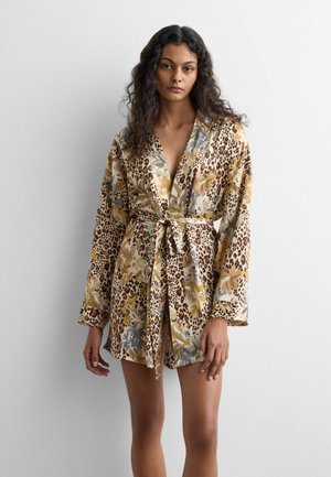 Femme aux longs cheveux bouclés portant une robe ceinturée à manches longues avec un motif mêlé léopard et floral.