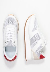 Bílo-šedé tenisky s prodyšnou textilií a jemným vzorem, se červenými akcenty, texturovanou podrážkou a polstrovaným límcem pro pohodlí.