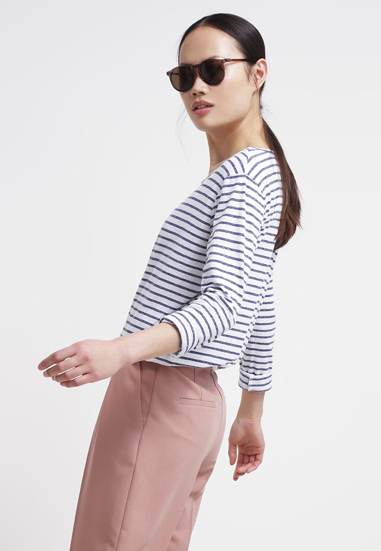 Gestreiftes Langarmhemd in Weiß und Marineblau, kombiniert mit hellrosa, taillierten Hosen. Das Modell trägt dunkle Sonnenbrillen.