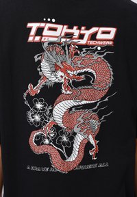 Fekete póló piros és ezüst sárkány grafikával, virágos elemekkel, valamint a "Tokyo Techwear" felirattal fehérben és pirosban.