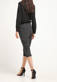 Musta paita ja harmaat leveälahkeiset housut, joissa on teksturoitu kangas. Asusteena kiiltävät mustat korkokengät.