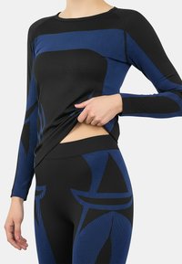 Black and blue activewear top with long sleeves, featuring a textured design and cut-out detail at the waist. Leggings with bold patterns.