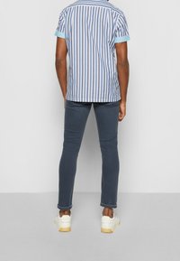 Camisa de manga corta a rayas en azul y blanco, combinada con jeans ajustados azul oscuro y zapatillas blancas con suelas texturizadas.