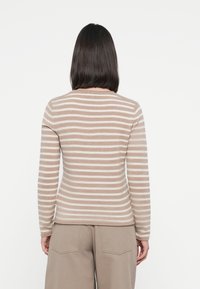 Sweter w paski z naprzemiennymi jasnobeżowymi i białymi paskami, długimi rękawami, okrągłym dekoltem oraz dopasowanym krojem. Wykonany z miękkiego, przytulnego materiału.