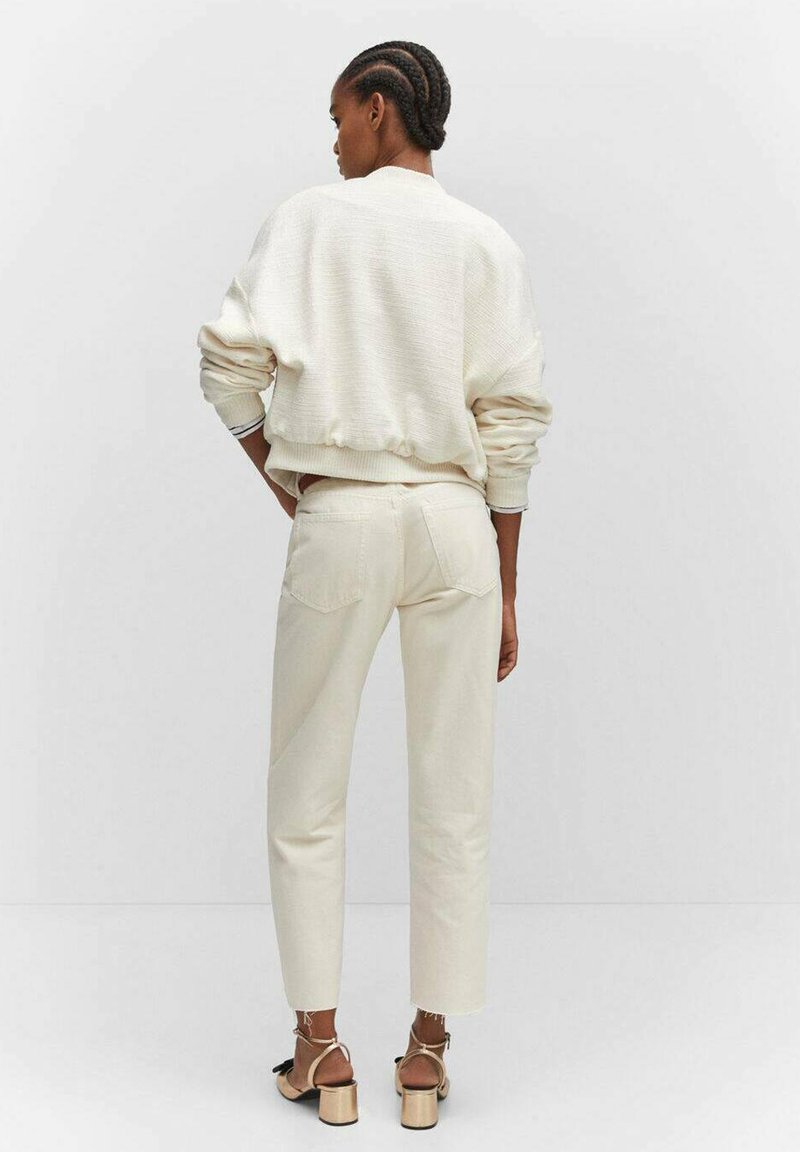 Cremefarbener Pullover mit Struktur und gerippten Bündchen, kombiniert mit cremefarbenen geraden Hosen. Der Look wird durch beigefarbene Riemchenschuhe abgerundet.