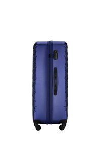 Hard-shell suitcase, deep blue, featuring a textured surface, vertical grooves, retractable handle, and four wheels for mobility.