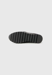 Semelle de chaussure en caoutchouc noir avec des lignes de grip horizontales et un avant rond. Présente une marque en relief. Texture lisse avec une légère traction.