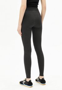 Grijze legging met een hoge tailleband, rekbare stof en een gladde textuur, gecombineerd met zwarte sportschoenen met witte en blauwe accenten.