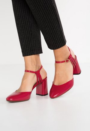 Rode leren hakken met een afgeronde neus en een enkelbandje. De hak is chunky en vierkant, met een glanzende afwerking.