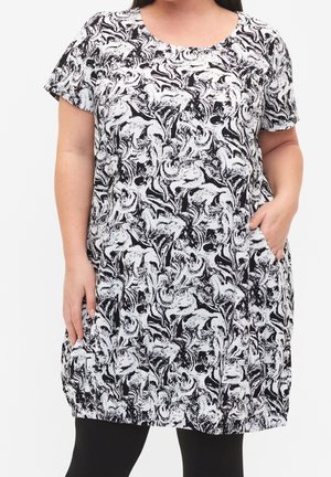 Femme grande taille portant une tunique à manches courtes à motif abstrait noir et blanc avec des poches, associée à un legging noir.