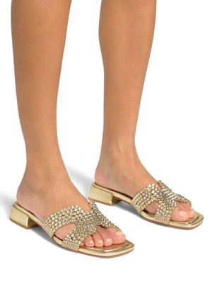 Goldene Riemchensandalen mit Blockabsatz, ausgestattet mit einem mit Juwelen verzierten Kreuzriemendesign und freiliegenden Zehen. Glatter metallischer Finish mit einem strukturierten Muster.