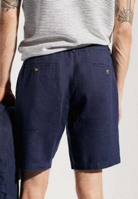 Shorts en lin bleu marine présentant une coupe classique, des poches arrière à boutons et un ourlet cousu. Texture lisse, design léger et respirant.
