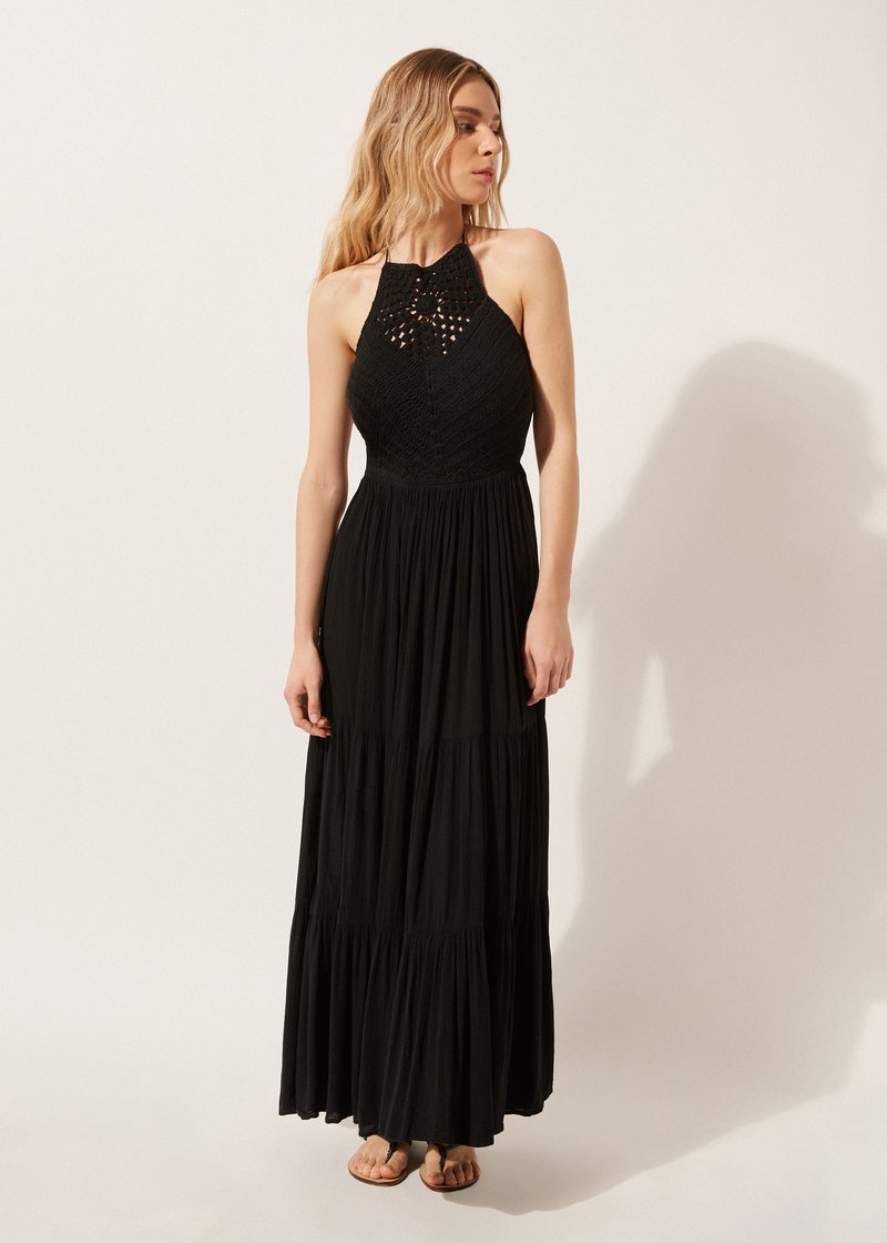 Vestido maxi negro con cuello halter, cuerpo texturizado y diseño de falda de volantes. Tela ligera con una silueta fluida y acentos minimalistas.