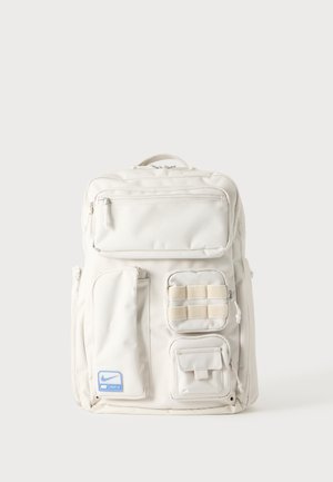 Sac à dos blanc Nike avec plusieurs poches zippées et compartiments, y compris un patch Nike bleu en bas à gauche.