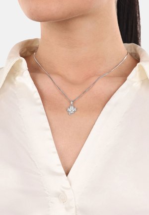 Collier pendentif en argent en forme de trèfle à quatre feuilles porté sur le cou d'une femme portant une chemise blanche à col.