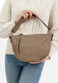 Borsa in pelle beige dalla forma curvata, con una tracolla nera, chiusura con zip e un piccolo accento con il marchio sul davanti.