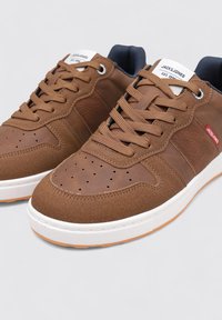 Baskets marron avec une texture en cuir lisse et en daim, bout perforé, semelle en caoutchouc blanche et intérieur bleu marine contrastant, dotées de lacets plats.