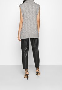 Suéter sin mangas de punto trenzado en gris, con cuello alto y dobladillo acanalado, combinado con pantalones de imitación cuero negros y sandalias de tacón alto negras con tiras.