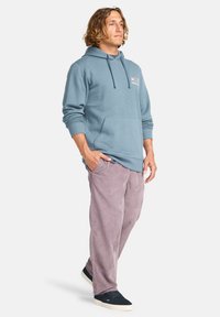 Light blue cotton hoodie with front pocket and drawstring hood, paired with light purple corduroy pants and black sneakers.