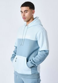 Sudadera azul clara con un diseño de bloques de color, que incluye un gran bolsillo frontal, capucha con cordones y un logo bordado en el pecho y la manga.