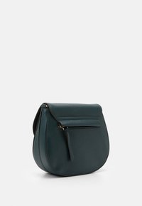 Sac à main en cuir turquoise avec une forme arrondie, fermeture zippée en haut et un pompon en cuir détachable. Présente des coutures contrastées et une texture lisse.