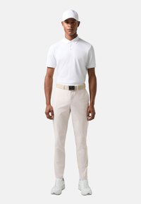 Biała koszulka polo, beżowy pasek, beżowe spodnie i białe tenisówki. Gładka faktura, dopasowany krój, krótkie rękawy i klasyczny kołnierzyk. W zestawie czapka z daszkiem piłkarskim.