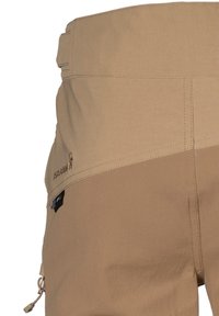Beige udendørsbukser med en tekstureret stof, der har et logo på taljebåndet, en lynlås lomme og forstærkede sømme langs sømmene.