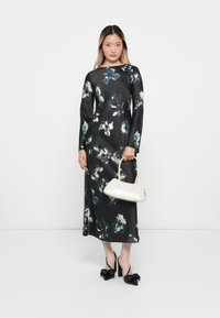 Long-sleeved black dress with green and blue floral print, smooth fabric, worn with a white handbag and black heeled shoes with bows.