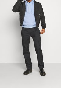Giubbotto bomber nero, felpa con cappuccio azzurro chiaro, pantaloni scuri e stivali neri. Il bomber ha una texture liscia con tasche frontali e una cerniera.