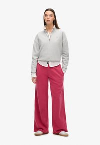 Szara bluza na zamek z wysokim kołnierzem, noszona na białej koszulce, w połączeniu z luźnymi, jaskrawo różowymi spodniami dresowymi i białymi trampkami.