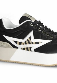 Zapatilla negra con suela de plataforma, con un diseño de estrella blanca, detalles en dorado y una franja con patrón. Cintas negras y tela texturizada.