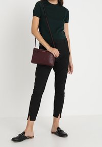 Mörkgrön kortärmad stickad topp, svarta smalpassande byxor med sidofickor, svarta slideskor och en liten vinröd lädercrossbody-väska.