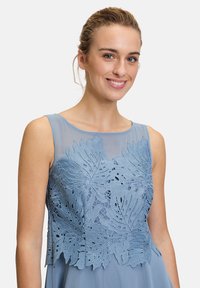 Hellblaues ärmelloses Kleid mit gesticktem Blattmuster im Oberteil. Weicher Stoff, runder Ausschnitt und geschichteter Saumdetails.