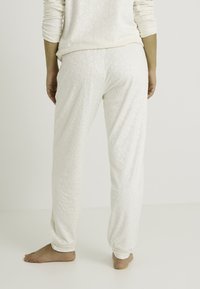 Pantalon de pyjama blanc avec un subtil motif léopard, en tissu doux, doté de poignets élastiques et d'une coupe décontractée, vu de dos.