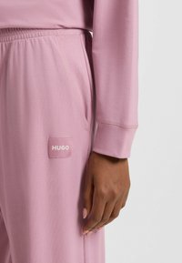 Pigiama con cintura elastica rosa caratterizzato da un discreto logo. Tessuto liscio con maniche lunghe e un fit rilassato.