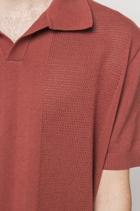Polo roșu cu mânecă scurtă, având un model plisat texturat pe o parte și țesătură netedă pe cealaltă. Design cu guler și margini striate.