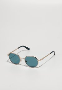 Occhiali da sole in metallo dorato con lenti blu, forma ovale, montatura sottile, dettagli verde scuro sulle tempie e noccioli trasparenti.