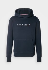 Sweat à capuche bleu marine avec poche kangourou avant et texte blanc « HILFIGER NEW YORK » avec des accents rouge, blanc et gris sur la poitrine.