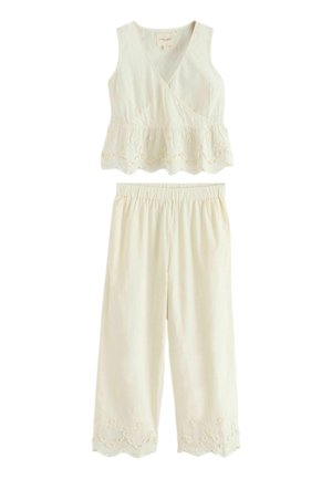 Ärmelloses weißes Crop-Top mit V-Ausschnitt und gezacktem Spitzenabschluss am Saum, kombiniert mit weit geschnittenen Hosen mit passender Spitzenverzierung an den Bündchen.