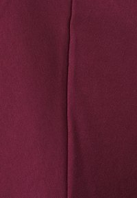 Das burgunderrote Gewebe zeigt eine glatte Textur mit feinen, diagonalen Webungen. Die Struktur hat eine Naht, die zwei Abschnitte teilt und Tiefe erzeugt.