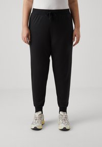 Joggers noirs fuselés avec taille à cordon, poignets côtelés et texture lisse, associés à des baskets de sport légères.