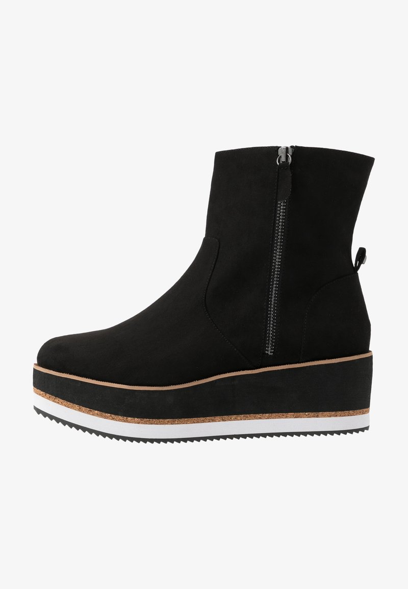 Bottine en suède noire avec fermeture éclair latérale, semelle plateforme épaisse avec des couches marron et blanches, et semelle extérieure noire texturée.