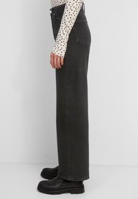 Vaqueros anchos de tiro alto en negro, fabricados en denim, que presentan un diseño clásico de cinco bolsillos con costuras en contraste y una textura suave.