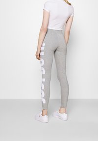 Grå leggings med vitt logotryck på vänster sida, tillverkade av en stretchig tyg. Kombineras med en åtsittande vit kortärmad topp.