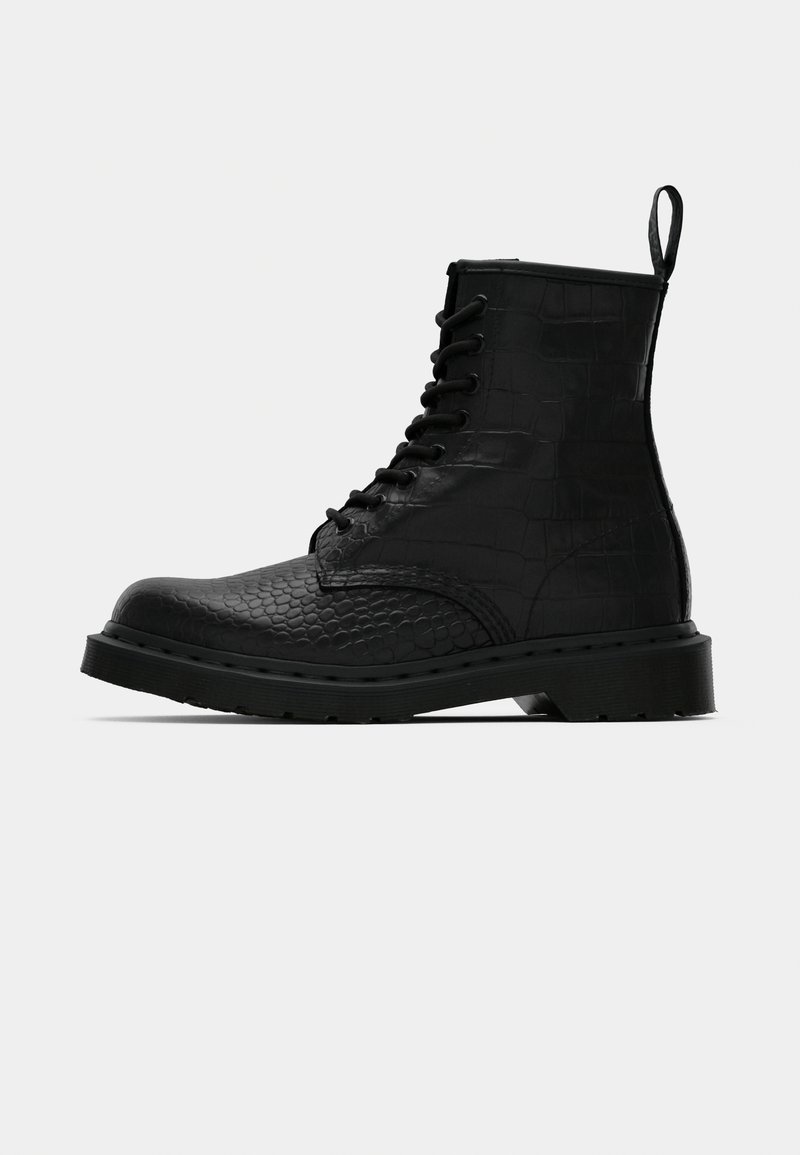 Bota de tobillo de cuero negro texturizado, con cordones y suela gruesa, con una pestaña en la parte posterior, mostrada de perfil contra un fondo liso.