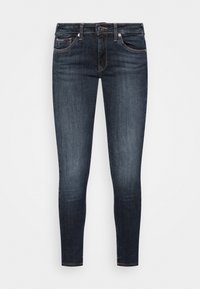 Jeans ajustados en denim índigo oscuro con una textura suave. Presenta cinco bolsillos y una clásica bragueta con botones. Minimalista, sin desgastes visibles.